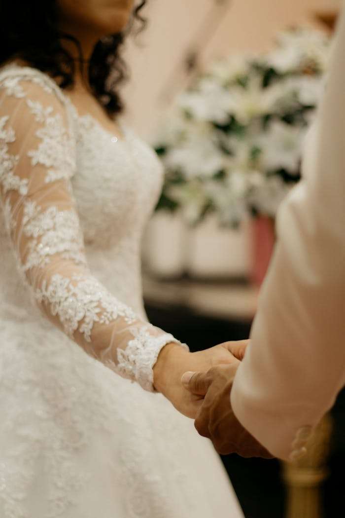 gallery-5 Elegant bride and groom holding hands during a touching wedding ceremony indoors.